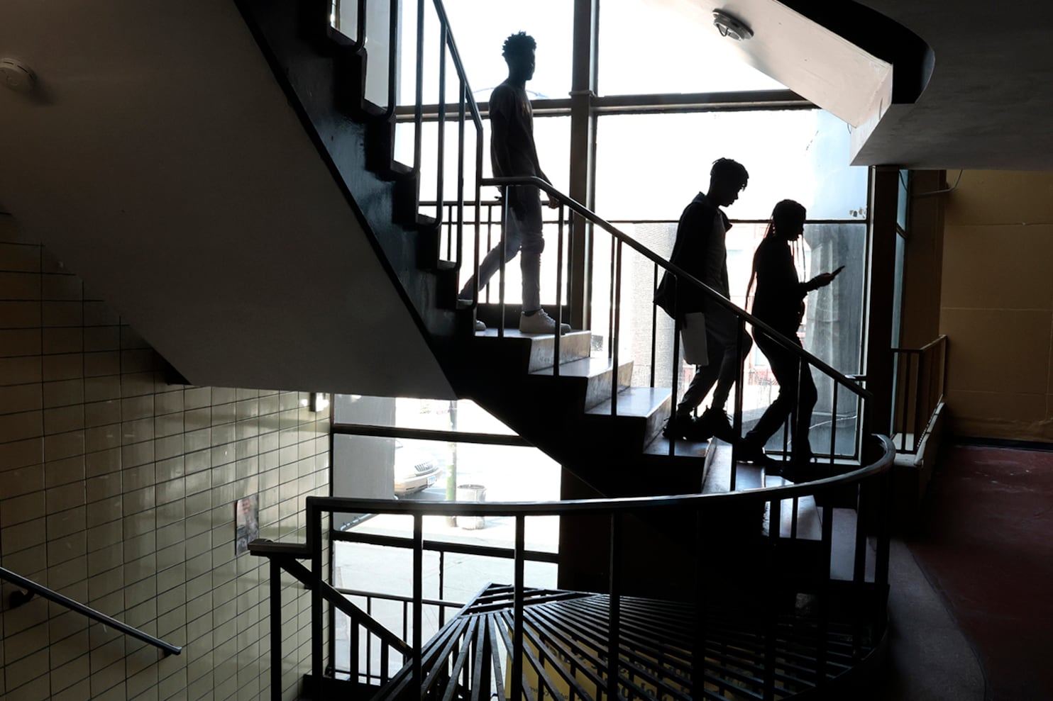 A silhouette of three high school students walking down the stairs in a high school building.