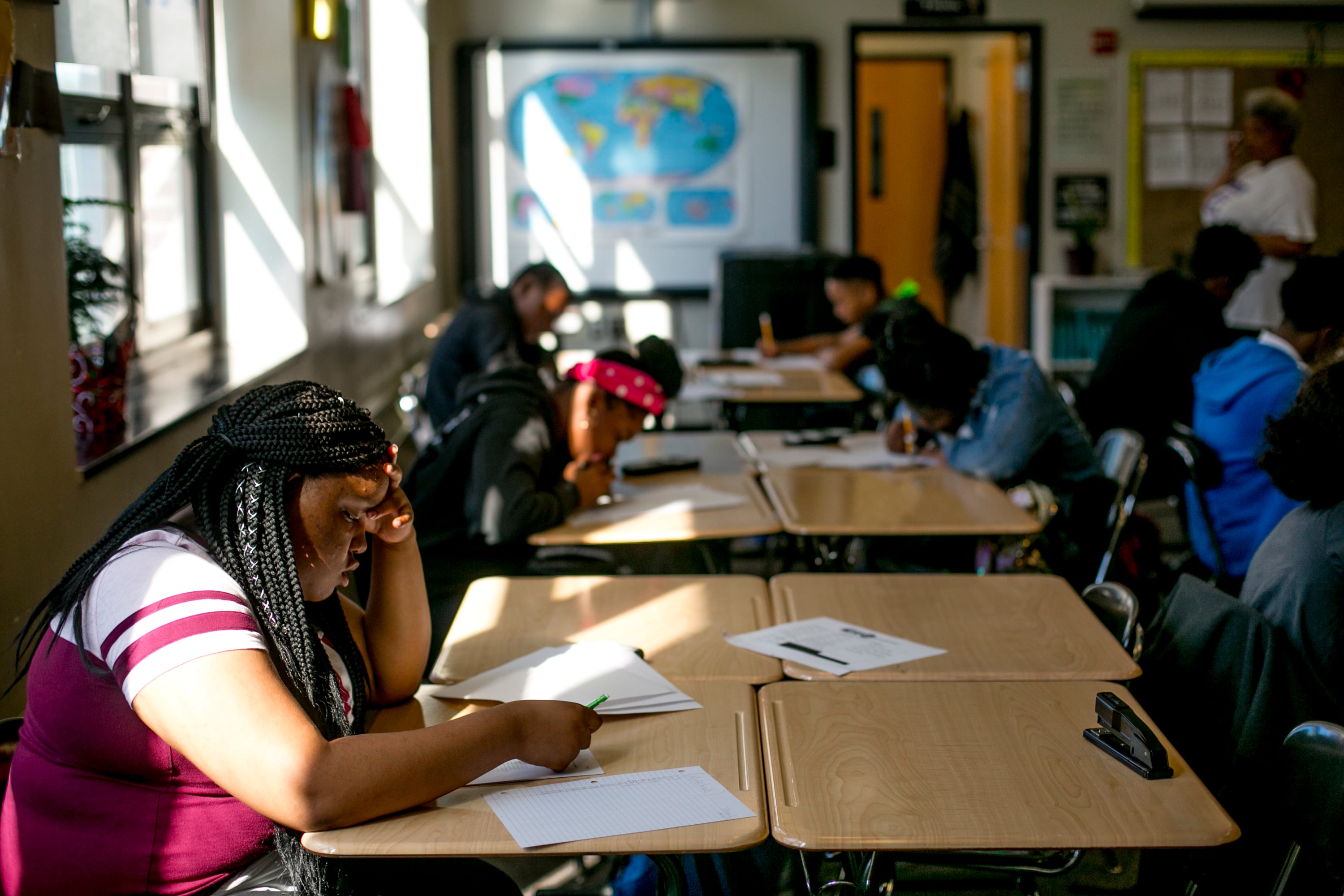 Students work at a long wooden desk in a classroom