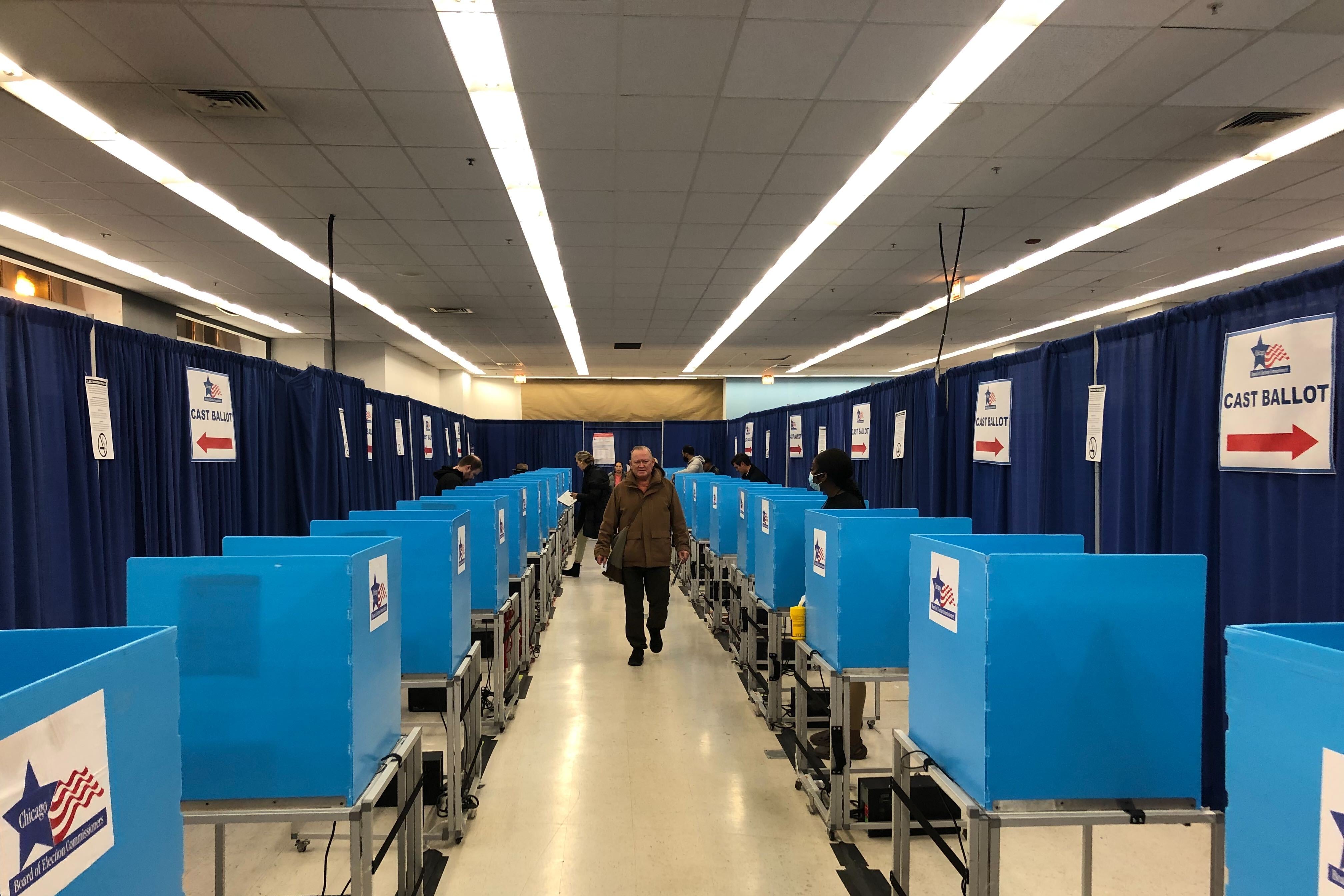 A person in a winter coat walks down a hallway of blue voting separators in a room.