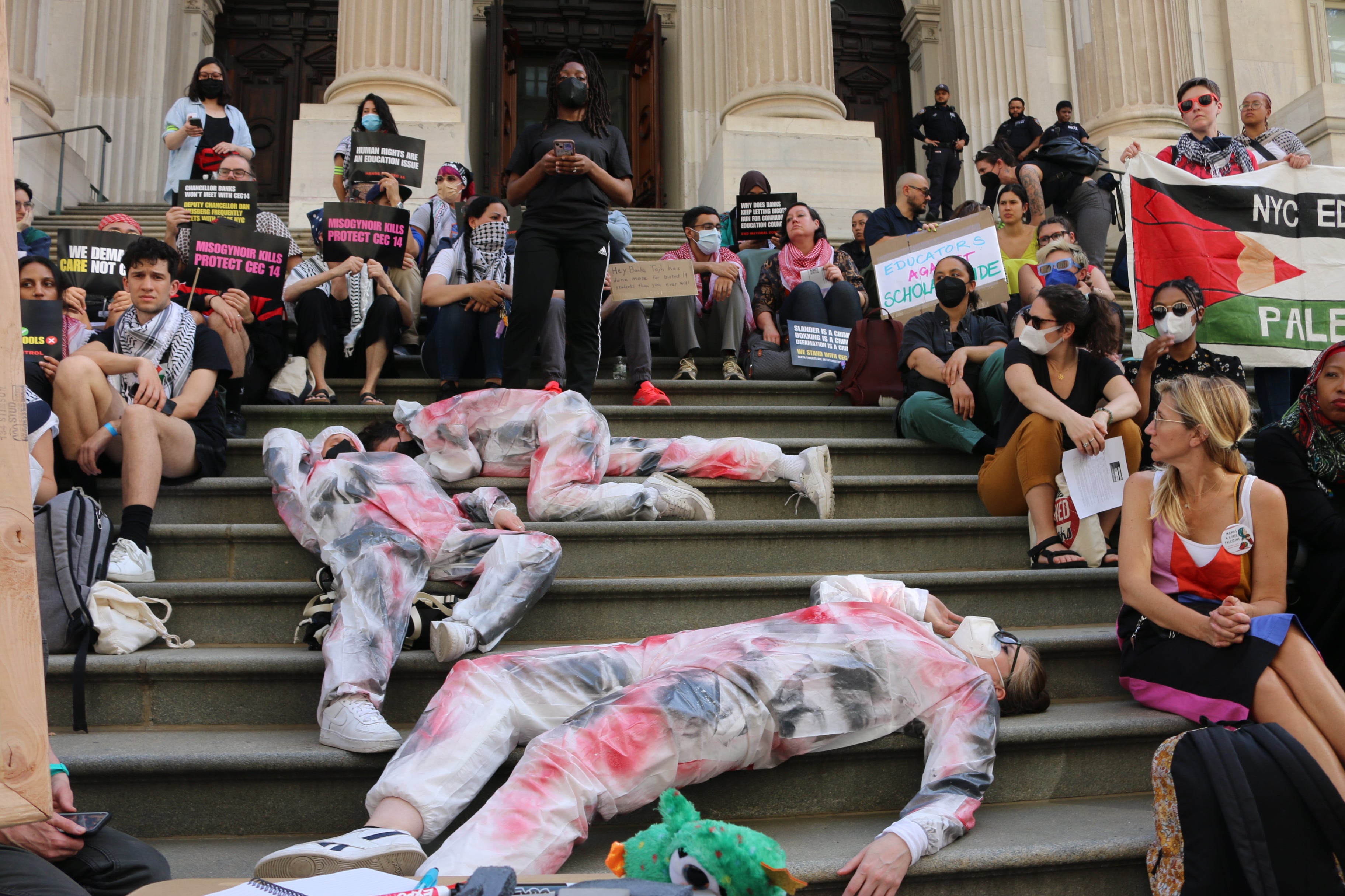 A group of people on steps including three in white jumpsuits with red and black paint on them.