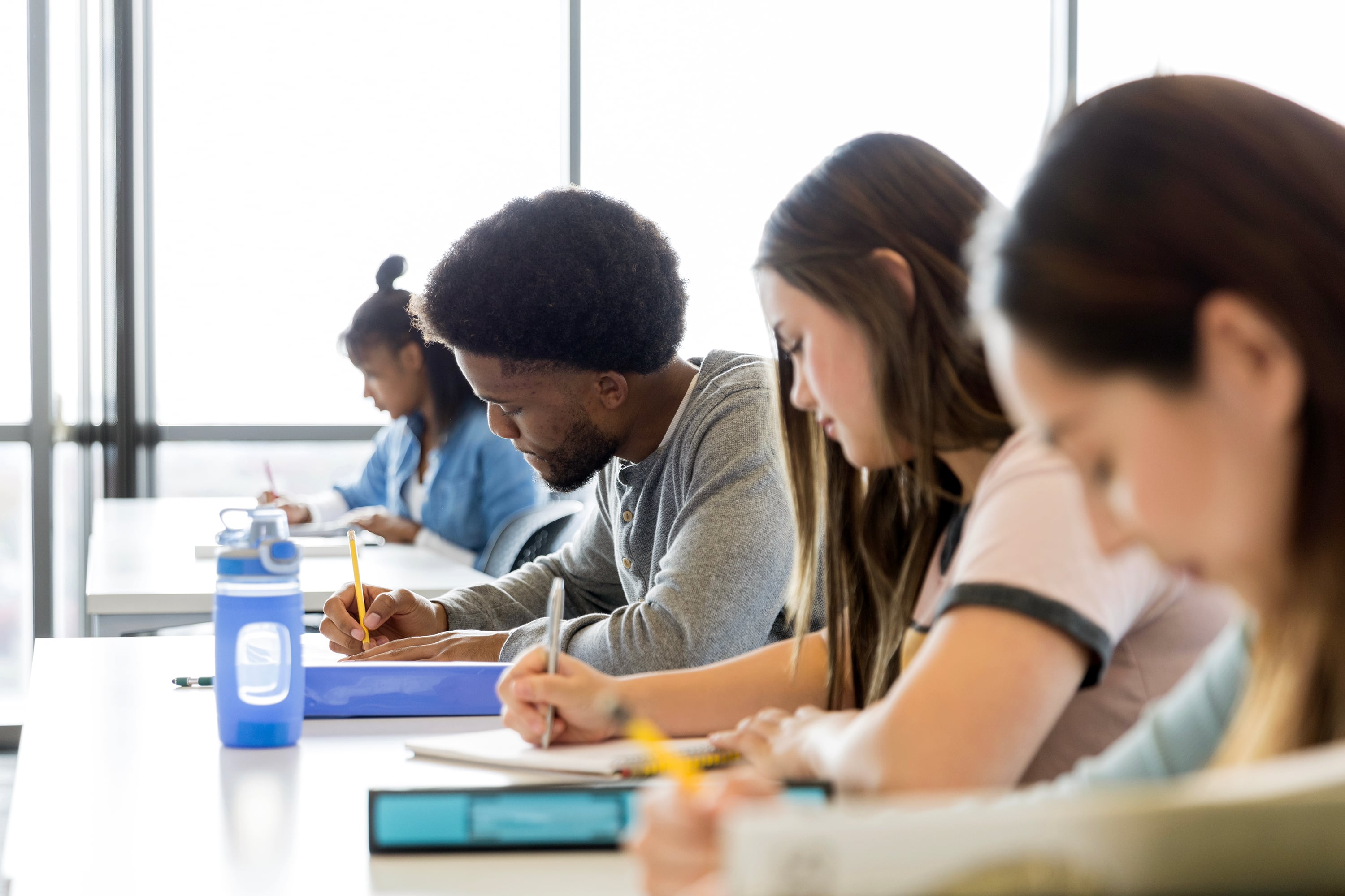 Four high school students sit in a row taking a test.