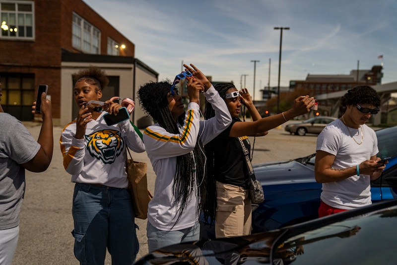 A group of high school students wear eclipse viewing glasses and look up at the sky.