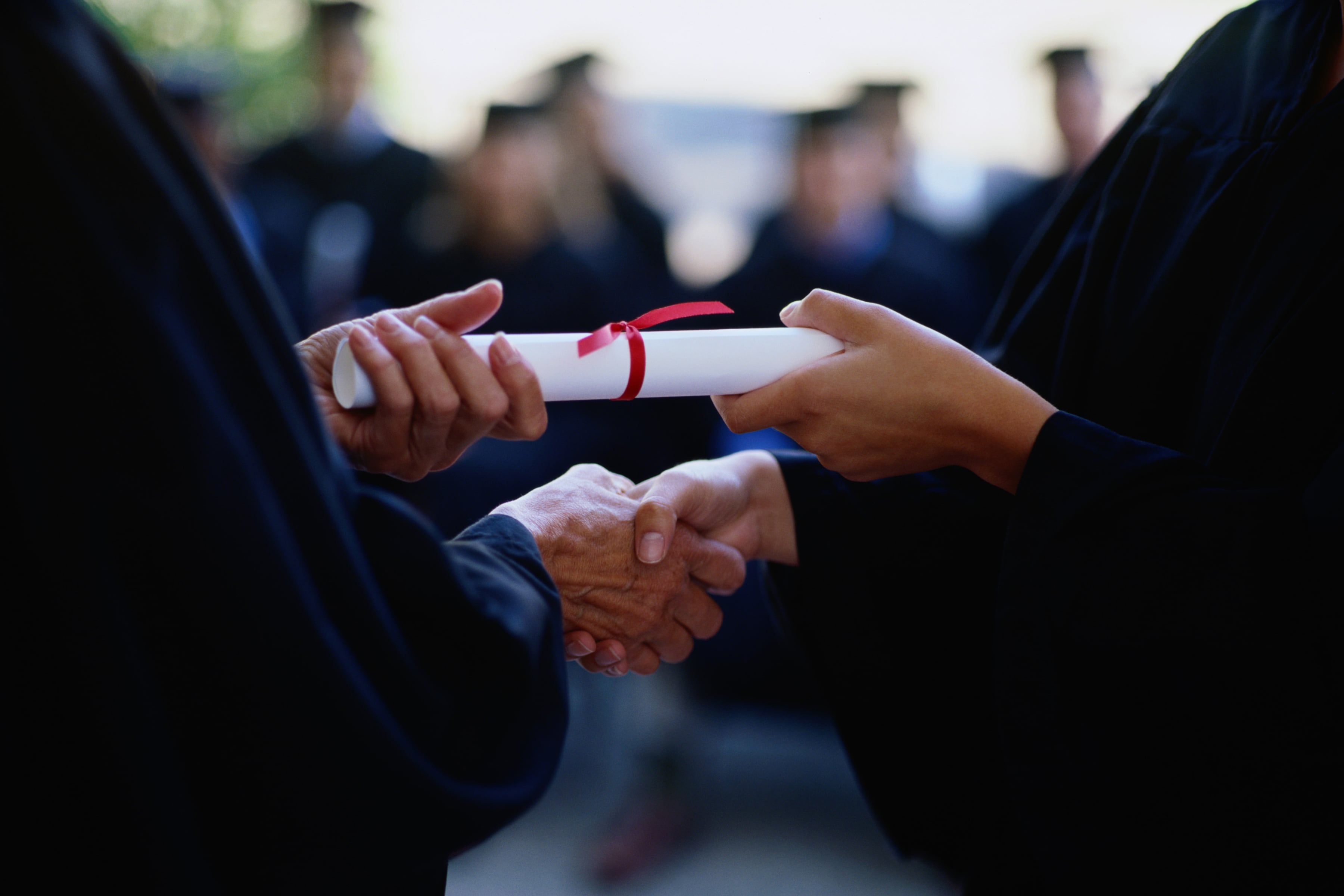 Two sets of hands shake and hold a school diploma.