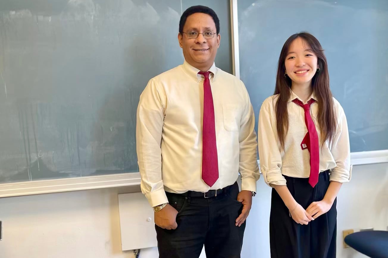 Man with red tie and female with red tie stand in front of a blackboard.