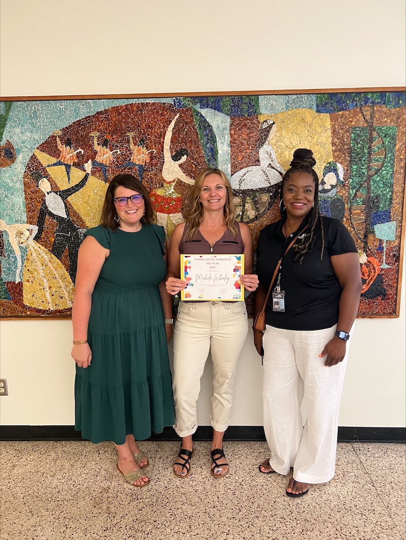 Three women stand in a line. The middle woman is holding a certificate