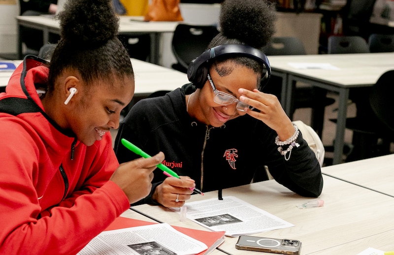 Two high school students work from a desk in a classroom.