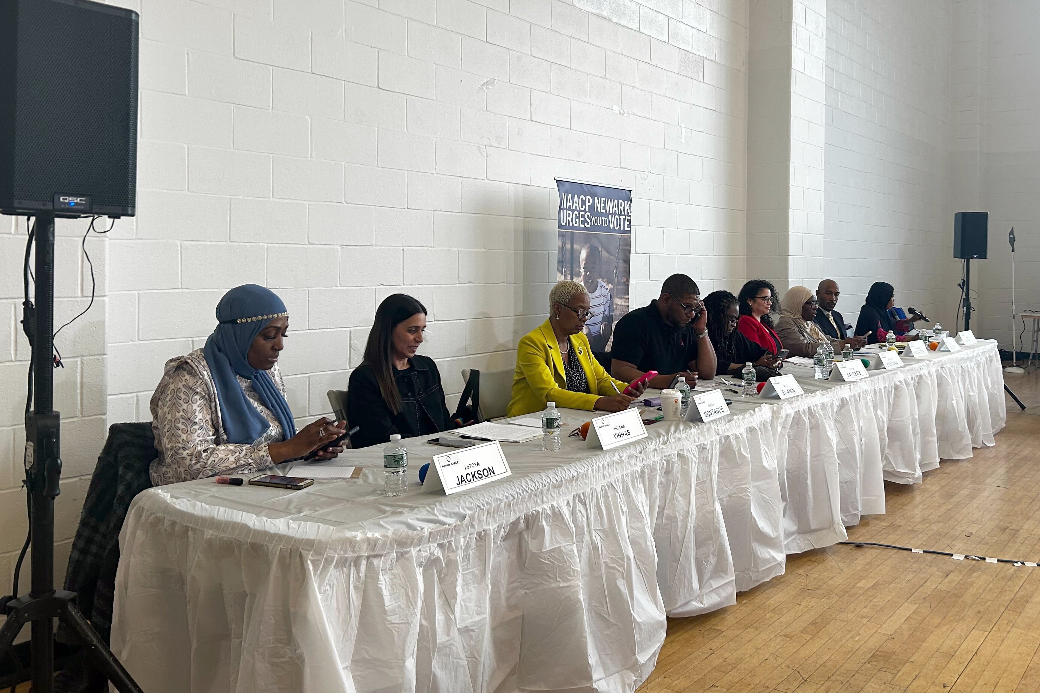 A row of people sit at a long, white table.