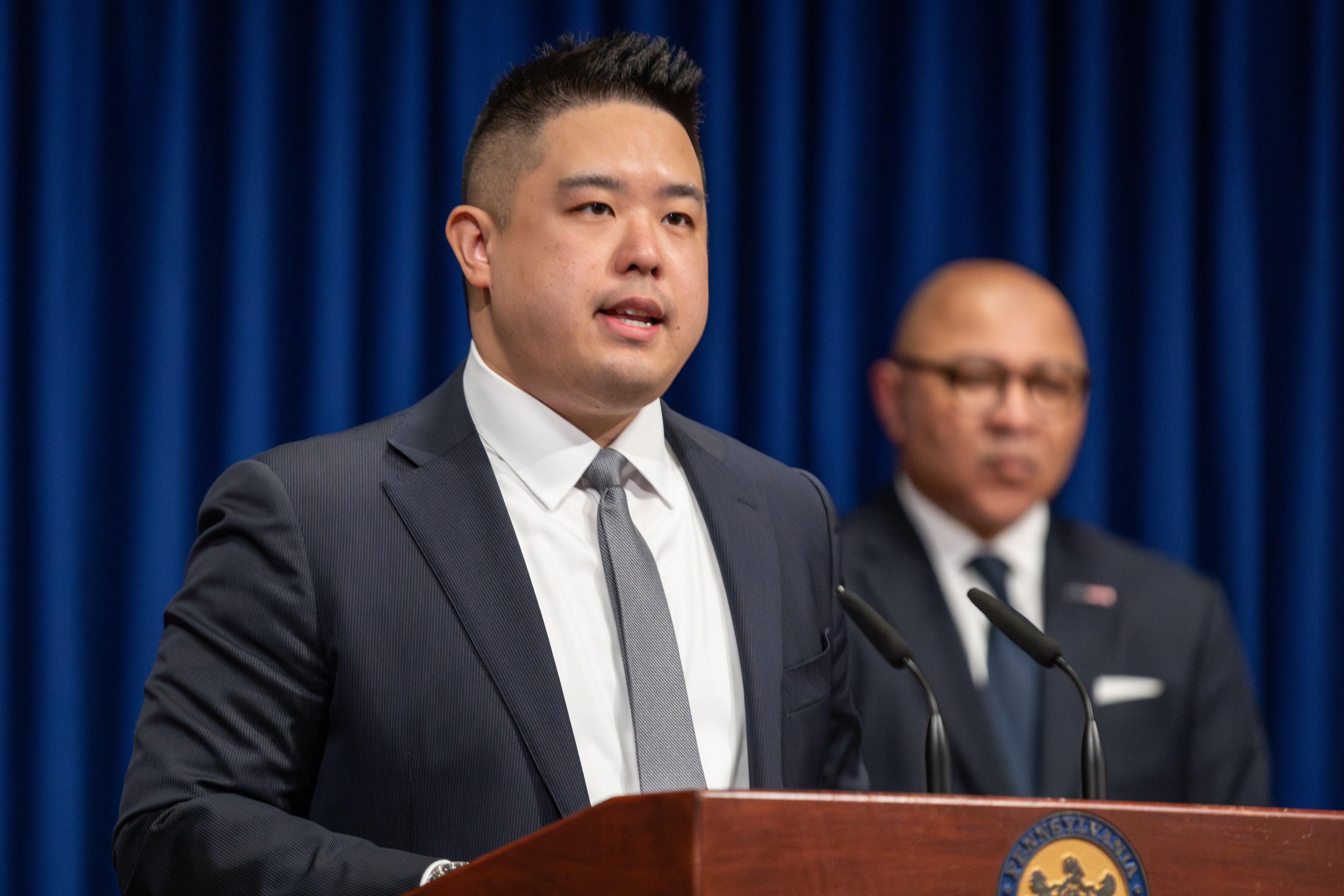 Philadelphia Charter School Office Director Peng Chao wears a suit and silver tie and speaks at a podium