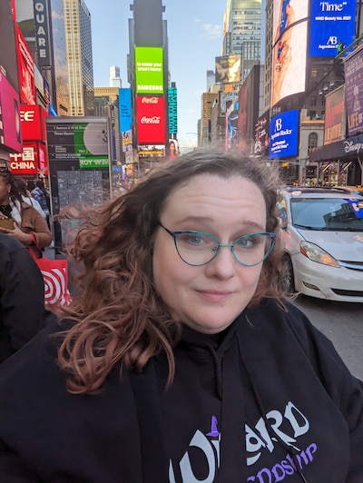 Headshot of a woman with light brown hair and classes standing in Times Square.