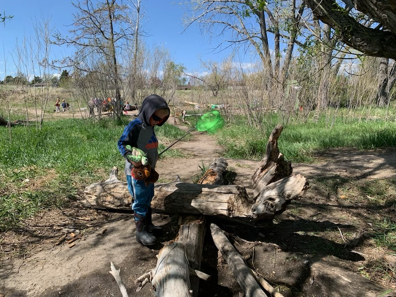 A child holds a stick while standing near a log outside.