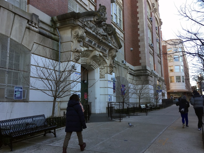 Three people walk on a sidewalk in front of a large stone school building.