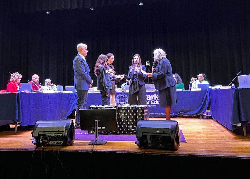 People stand on a stage with tables in the background.