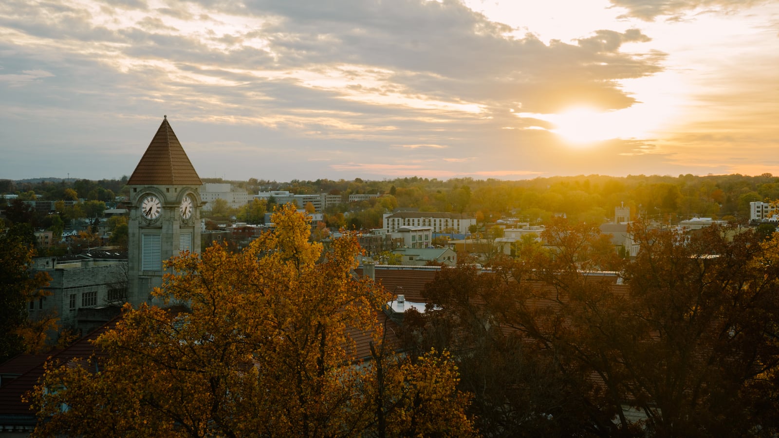 The sun shines over trees and buildings.