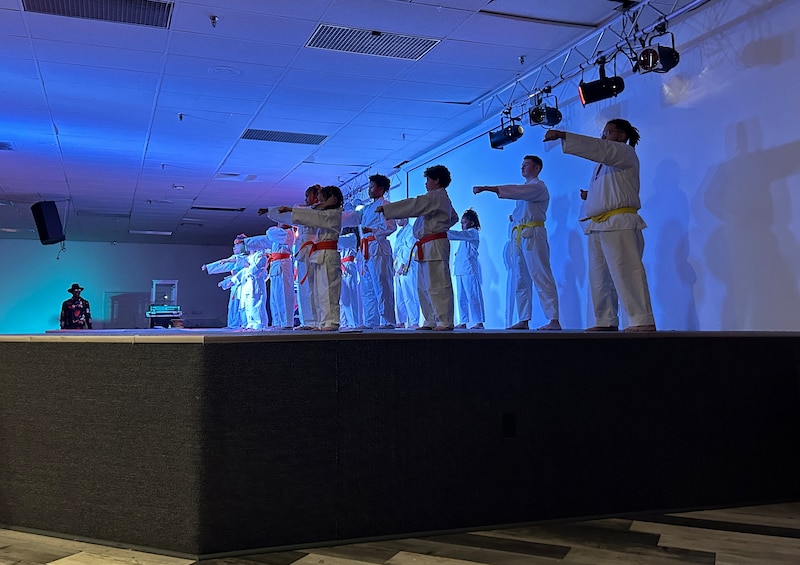 A group of young boys wearing all white uniforms stand on a stage during a ceremony.