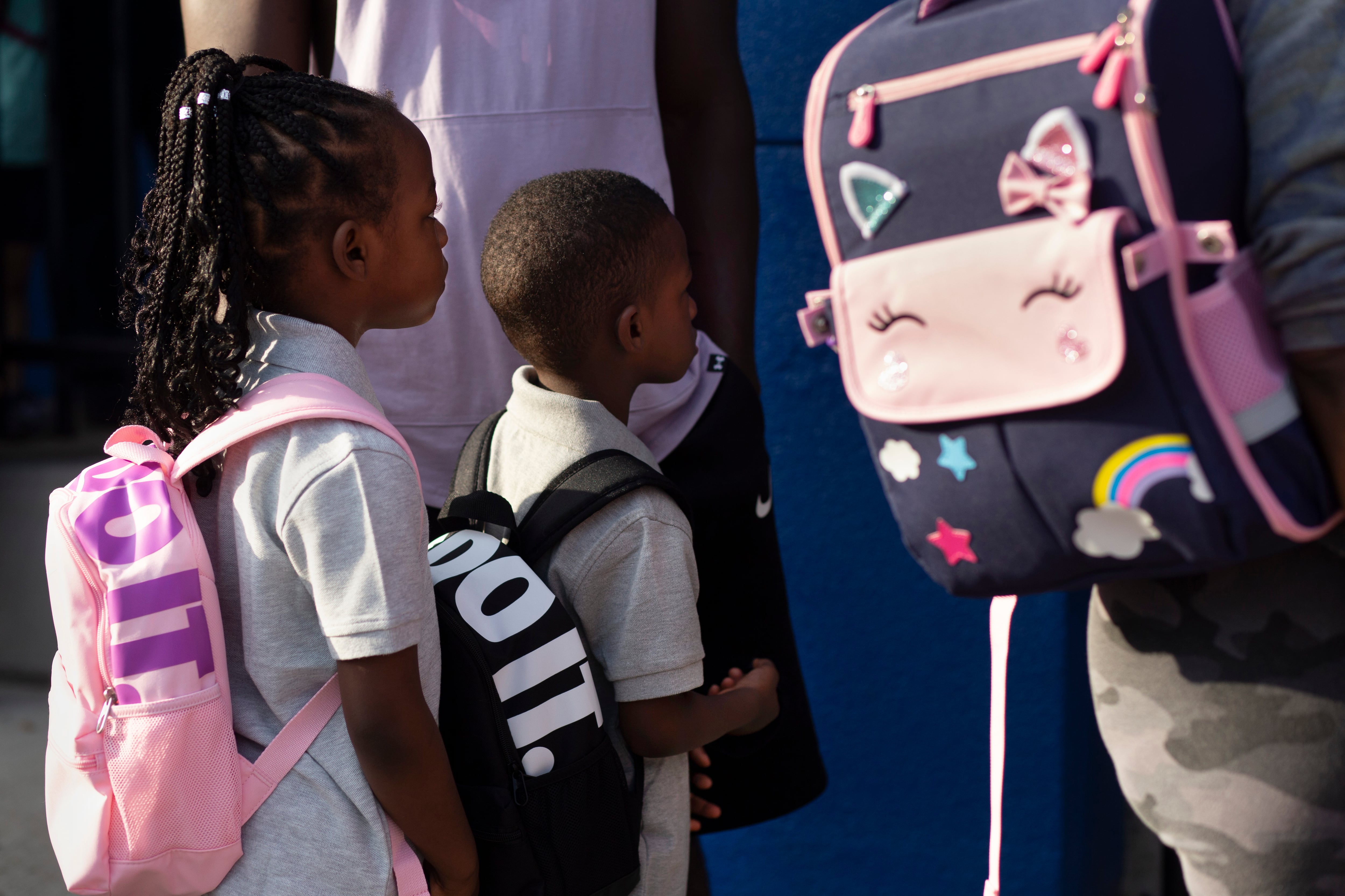 Two students dressed in their best for school and wearing backpacks, stand in line waiting to enter school on the first day.