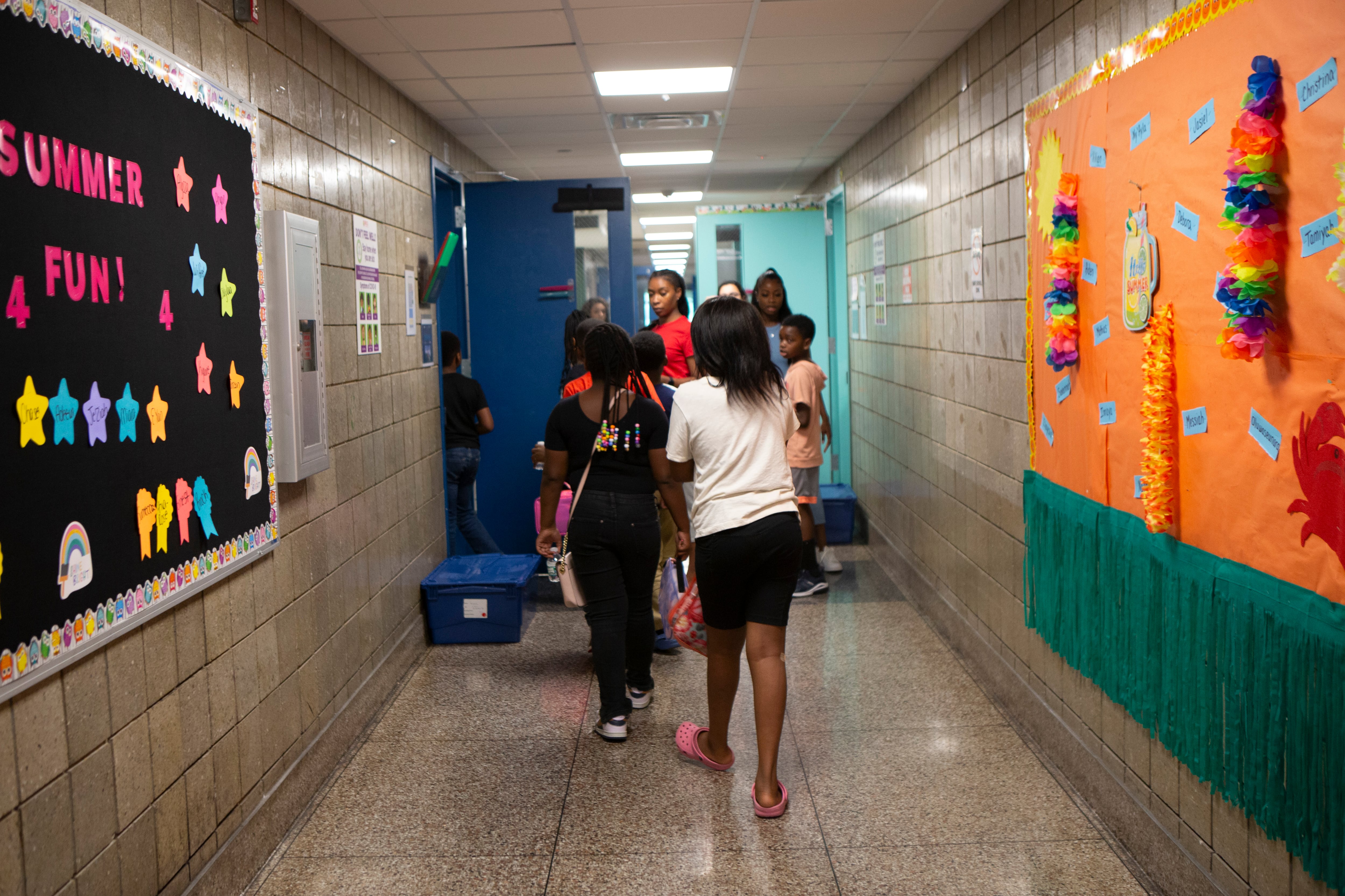 A group of  students and faculty walk down a hallway with posters and decorations on the walls.