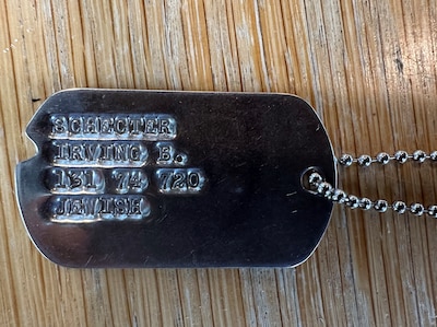 A military ID metal tag on a metal chain sits on top of a wooden table.