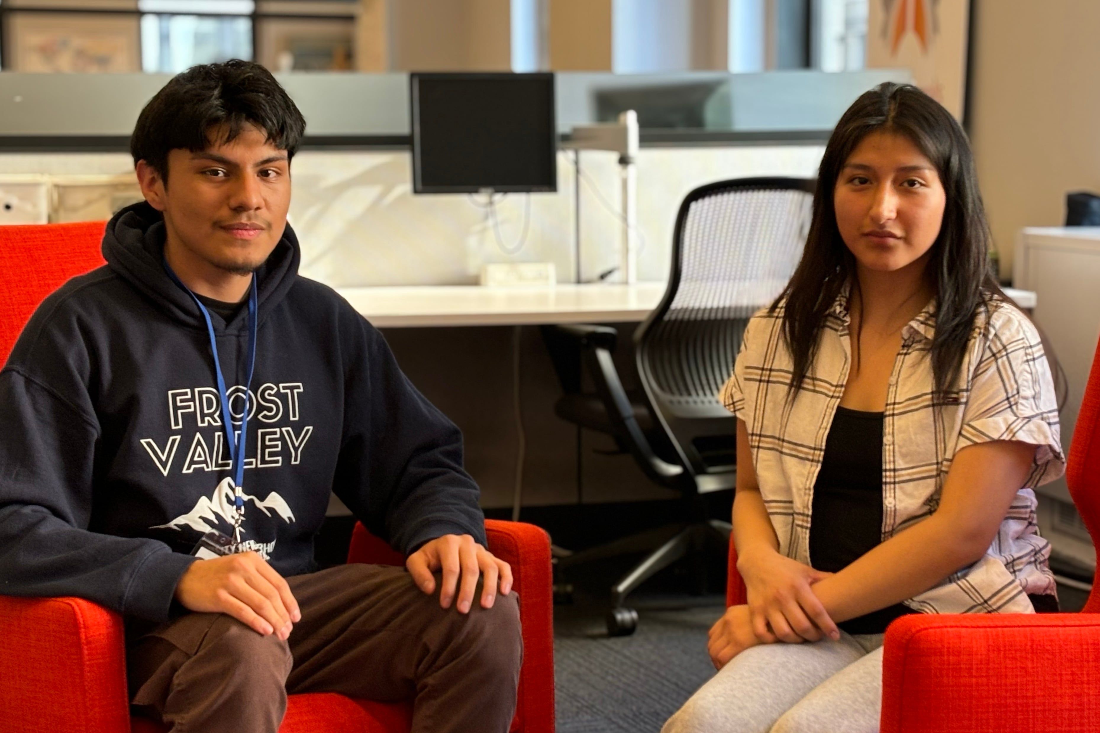 Two high school students sit next to each other on red chairs posing for a portrait.