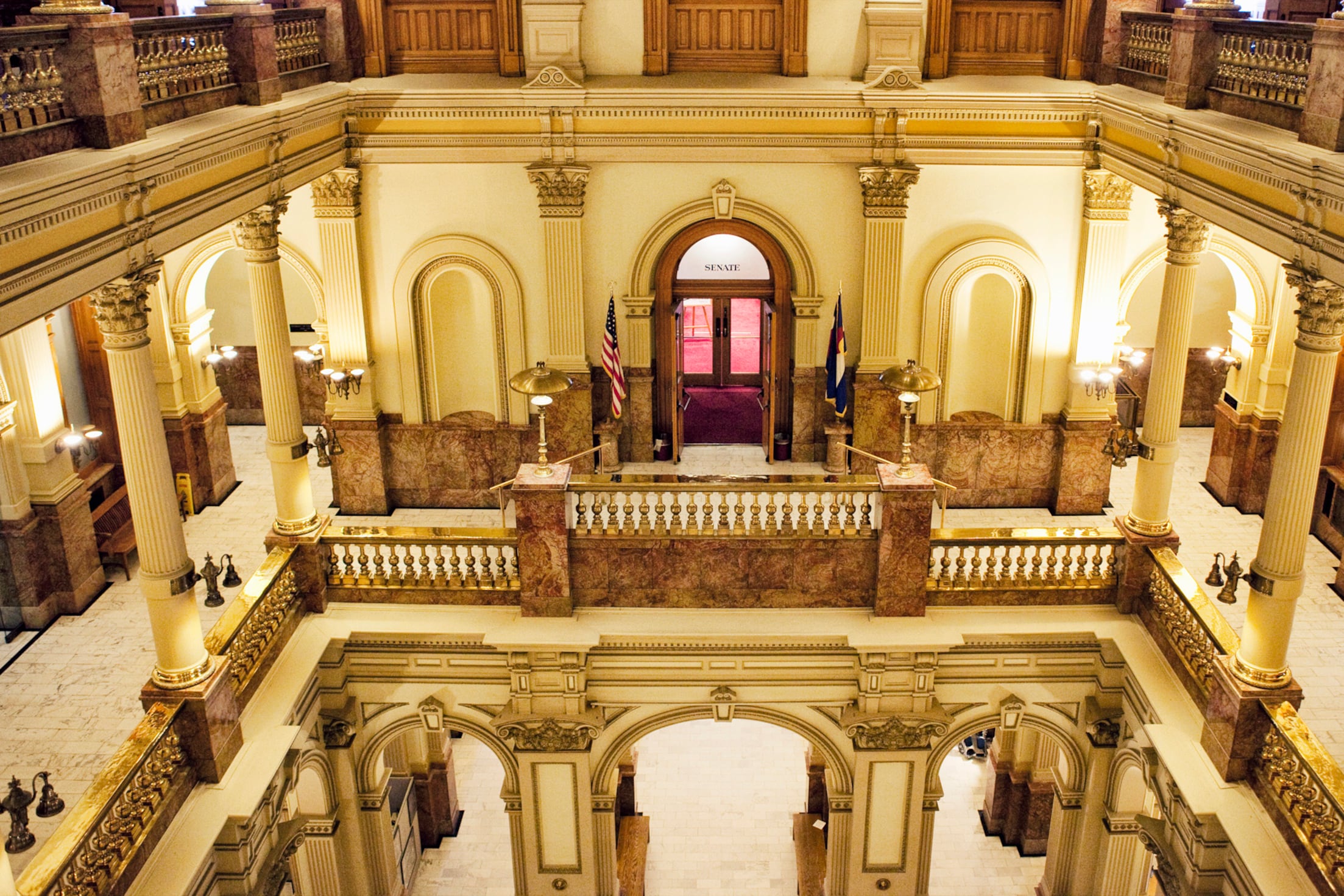 An inside view of the Colorado Capitol building with light stone walls and pillars and wooden doors and features.