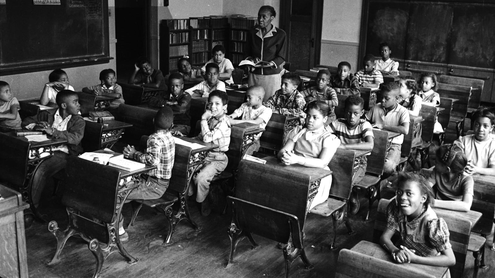 A black and white photo a teacher and a classroom full of students in a segregated school for Black children in 1953.