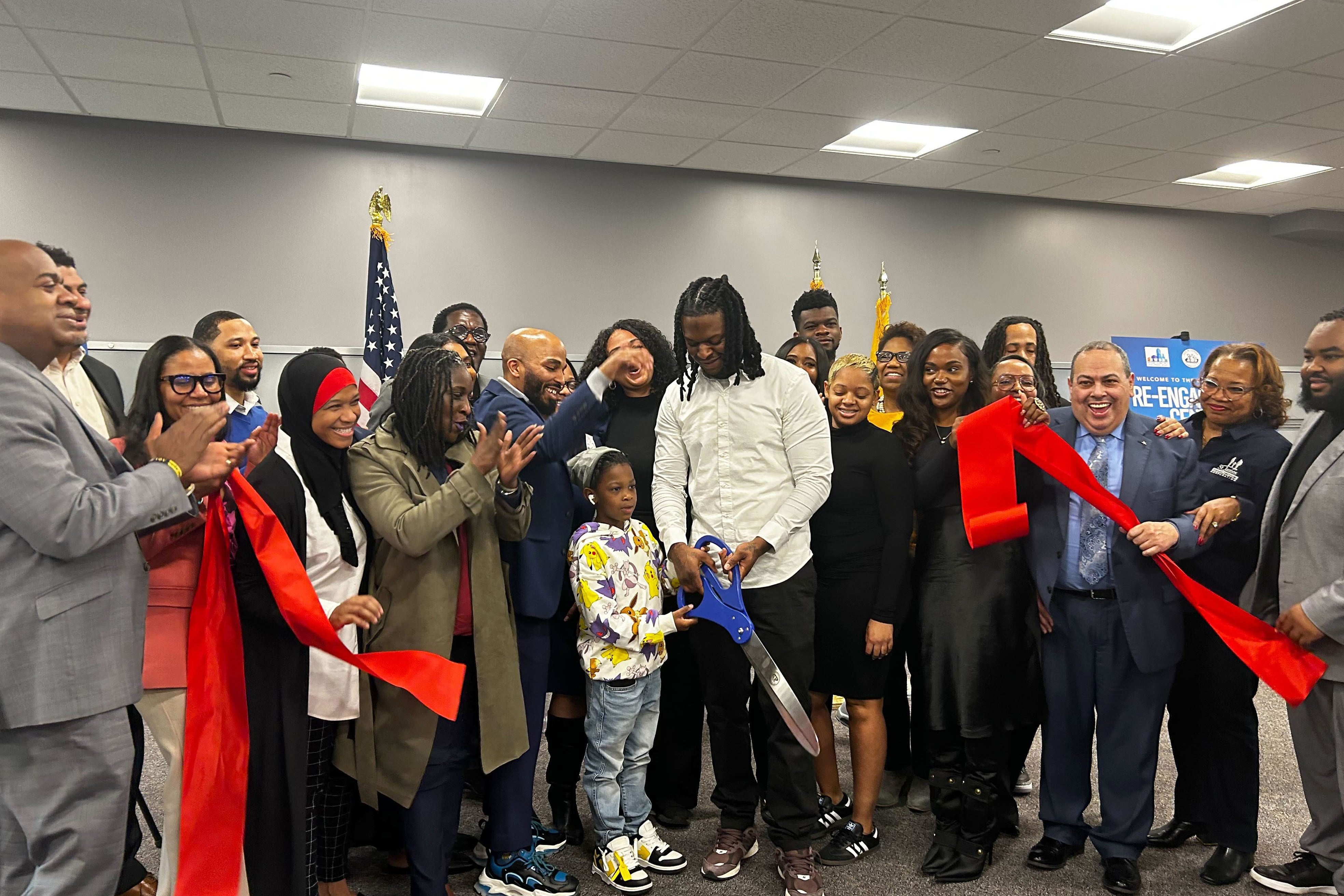 A group of people cheer while a person holds a giant pair of scissors after cutting a red ribbon.