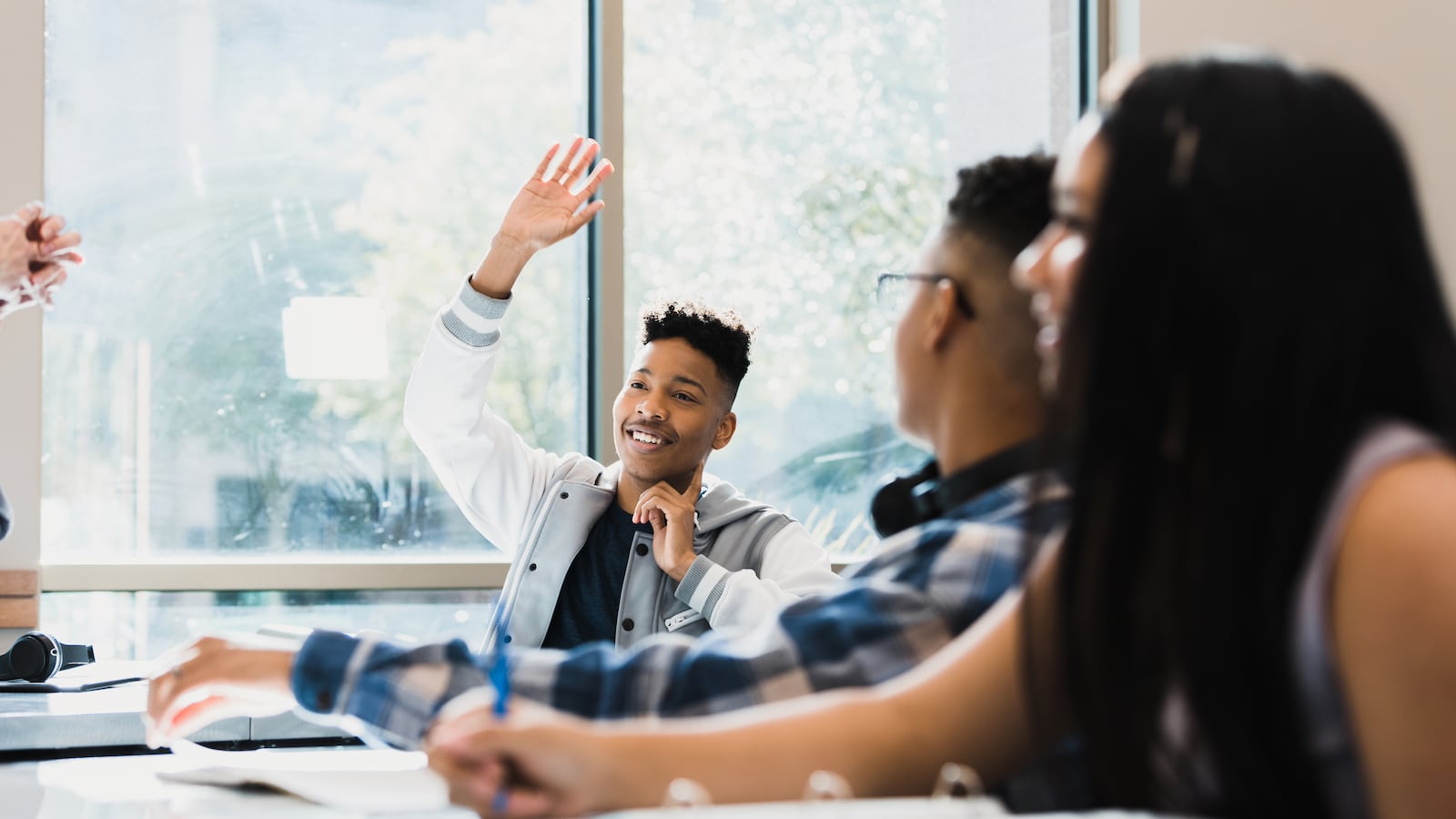 The teenage boy raises his hands and smiles as he entertains his classmates.