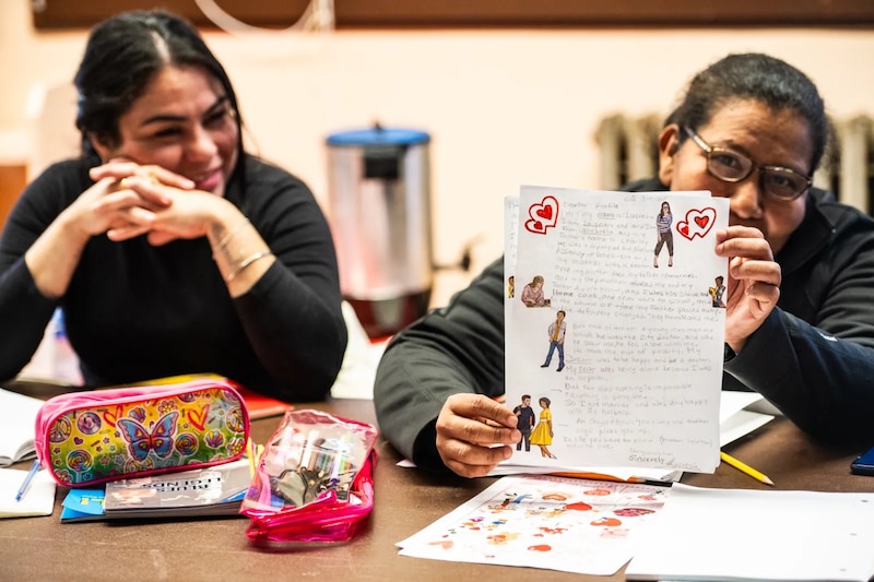 A woman holds up a piece of loose leaf paper. It's homework for the English as a Second Language class she takes at Lowell Elementary School in Humboldt Park in Chicago on March 7, 2024.