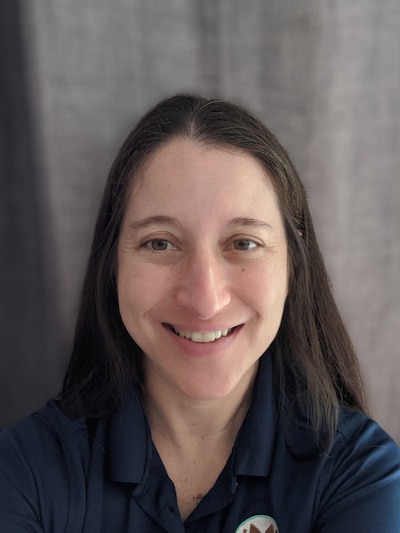 A person with long brown hair smiles while looking at the camera for a portrait.